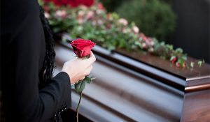 Woman holding a red rose in front of a casket with candles.