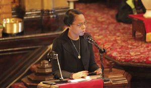 Woman at a podium during a funeral reading a eulogy.